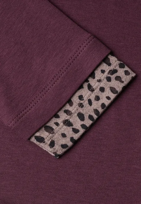 Bordeauxrotes Textil mit einem beigen Label, das schwarze, unregelmäßige Punkte zeigt.