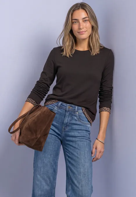 Langarm Shirt mit Colorblock und Printdetail black coffee Eine Frau trägt schwarzen Pullover, blaue Jeans und hält eine braune Tasche vor violettem Hintergrund.