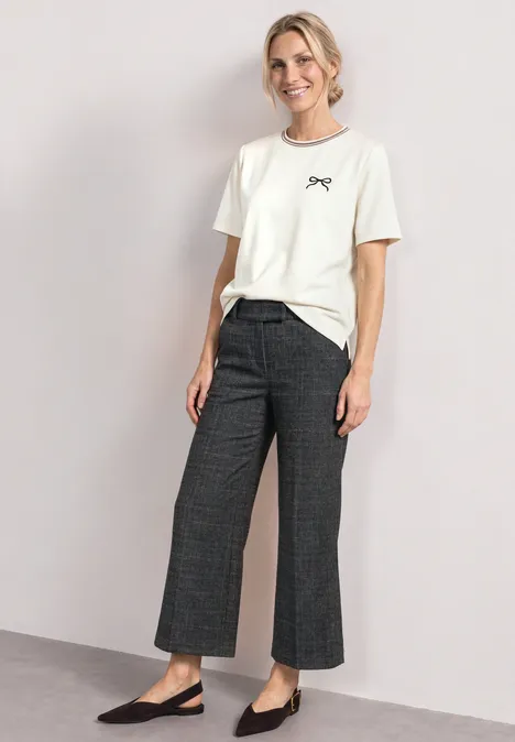 T-shirt à col rond avec détail brodé off white Frau trägt weißes T-Shirt, weite Karohose und schwarze Ballerinas vor hellem Hintergrund.