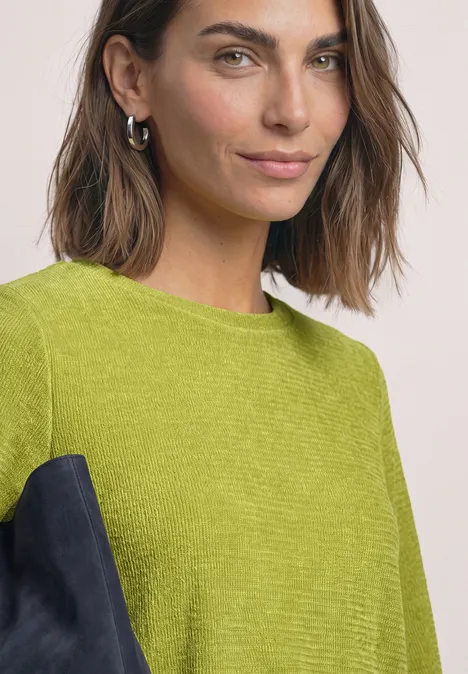 Porträt einer Frau mit braunen Haaren, die einen grünen Pullover trägt.