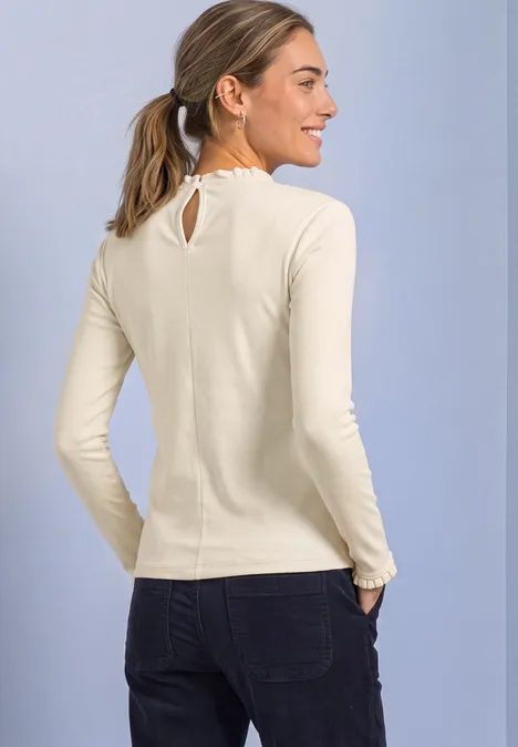 Een lachende vrouw in profiel met lichtbeige shirt, donkere jeans voor een lichte achtergrond.