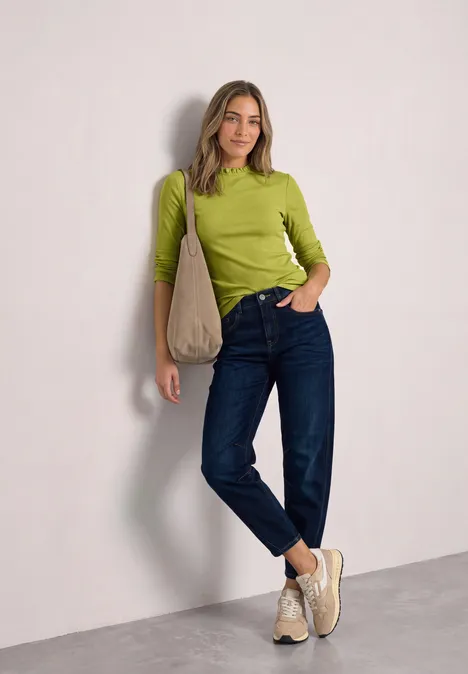 Vrouw in groene top, blauwe jeans en beige schoenen, casual met een schoudertas.