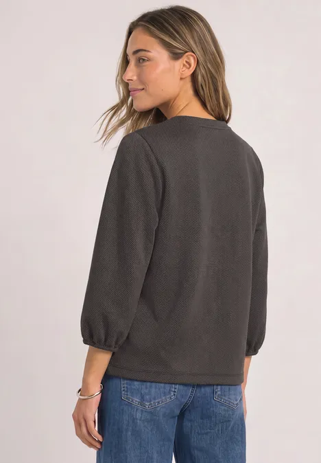 Eine Frau von hinten in dunkelgrauem Pullover mit dreiviertelarm und blauer Jeans.