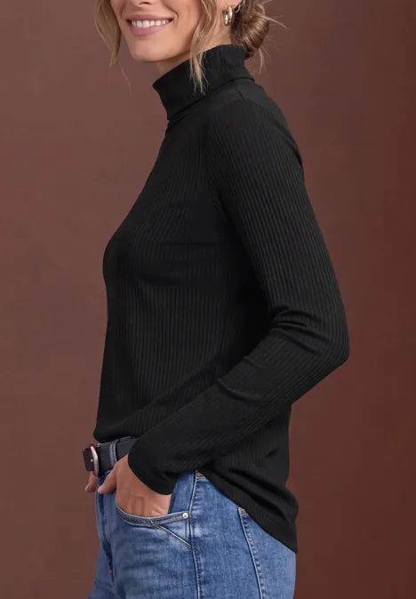 Frau im Profil in schwarzem Rollkragenpullover und blauen Jeans vor braunem Hintergrund.