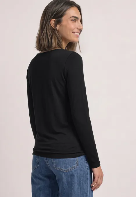 T-shirt basique à col bateau Black Junge Frau im Profil von hinten, trägt schwarzen Langarmshirt und Jeans, lächelt.