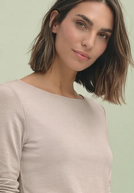T-shirt basique à col bateau clay sand Junge Frau mit schulterlangen Haaren und beigem Oberteil, leicht lächelnd vor schlichtem Hintergrund.