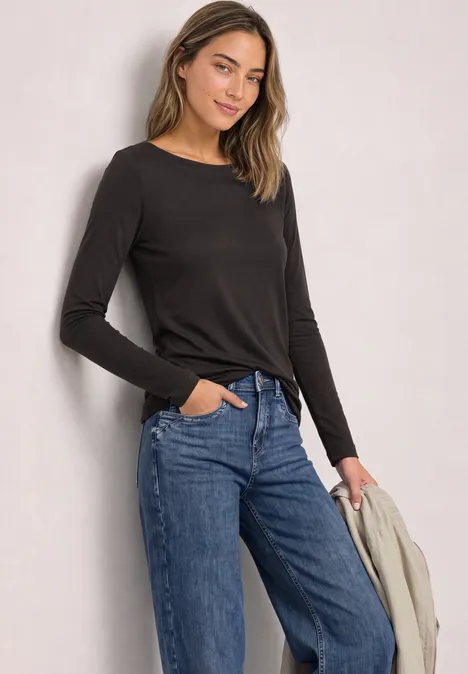 Basic Shirt mit U-Boot-Ausschnitt black coffee Junge Frau in schwarzem Langarmshirt und blauen Jeans hält eine helle Jacke in der Hand.