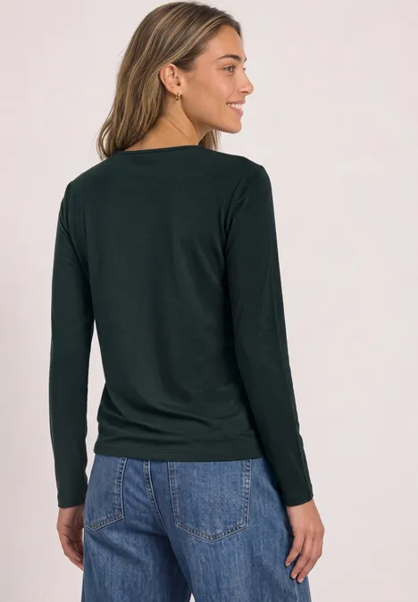 Vrouw van achteren in zwart shirt met lange mouwen en blauwe jeans, schuin staand.