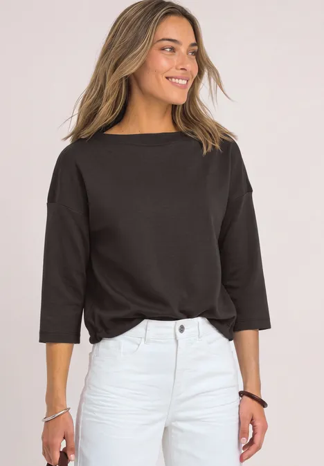 3/4-Arm Shirt mit Boat Neck und Tunnelzug black coffee Frau in schwarzem 3/4-Arm-Shirt und heller Hose, lächelnd vor hellem Hintergrund.