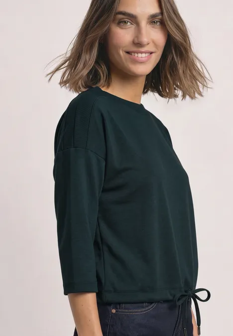 3/4-Arm Shirt mit Boat Neck und Tunnelzug stormy green Eine lächelnde Frau im schwarzen 3/4-Arm-Pullover mit Tunnelzug am Saum, in leichter Seitenansicht.