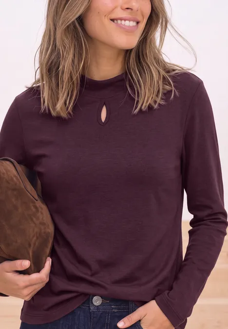 Vrouw in een donkerrood shirt met lange mouwen en klein sleutelgat bij de hals, met een bruine tas.