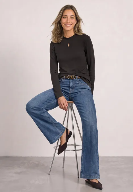 Shirt mit Turtle Neck und Schlitzdetail black coffee Blonde Frau in schwarzem Pullover und weiter Jeans sitzt entspannt auf einem Hocker