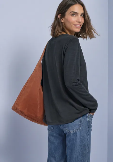 Vrouw in zwarte top en blauwe jeans kijkt over haar schouder, met een grote bruine schoudertas.