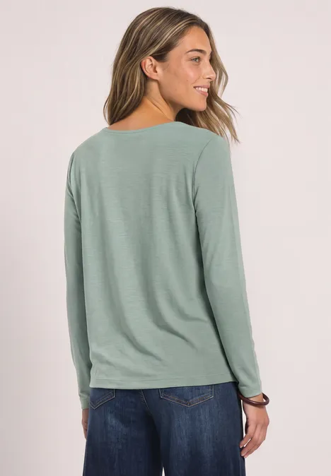 Zijaanzicht van een vrouw in een lichtgroene longsleeve en blauwe spijkerbroek.