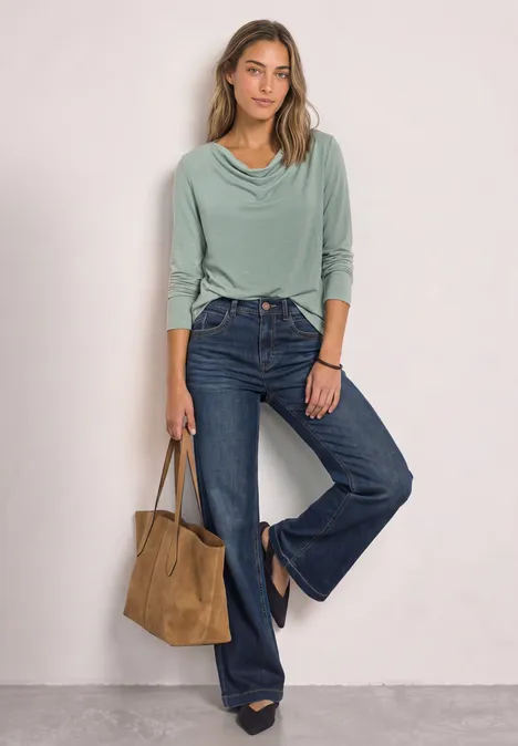 Vrouw in groene coltop en wijde jeans met hoge taille, draagt een bruine suède shopper en zwarte laarzen.