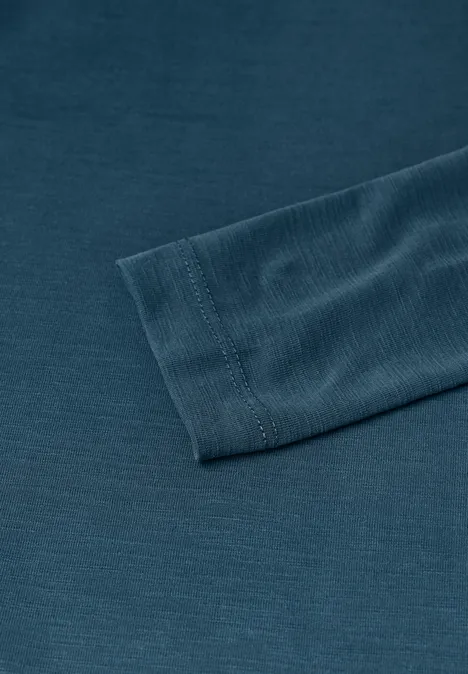 Close-up van een donkergroen shirt met lange mouwen en geribde manchetten, op een effen ondergrond.
