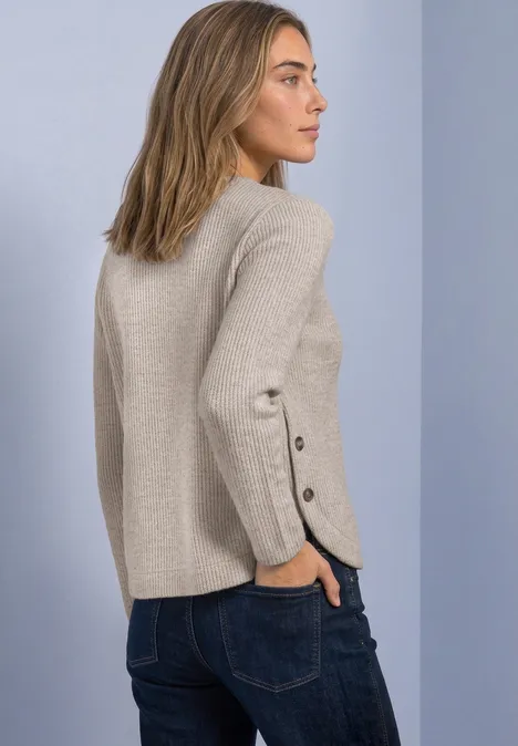 Langarm Shirt mit seitlichen Knopfdetails sanded amber mel. Frau im Profil trägt beigen Pullover mit Knopfdetails an den Ärmeln und Jeans.