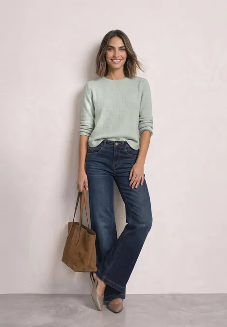 Langarm Shirt mit seitlichen Knopfdetails eucalyptus green mel. Eine Frau in grünem Pullover, weitem Jeans, High Heels und Wildledertasche vor neutralem Hintergrund.