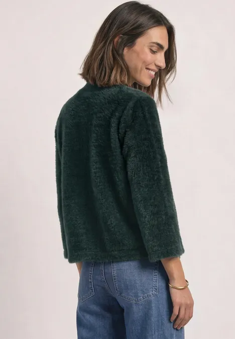 3/4-Arm Shirt mit Turtle Neck stormy green Frau mit mittellangen, braunen Haaren trägt grünen Kuschelpullover und blaue Jeans, lächelt zur Seite.