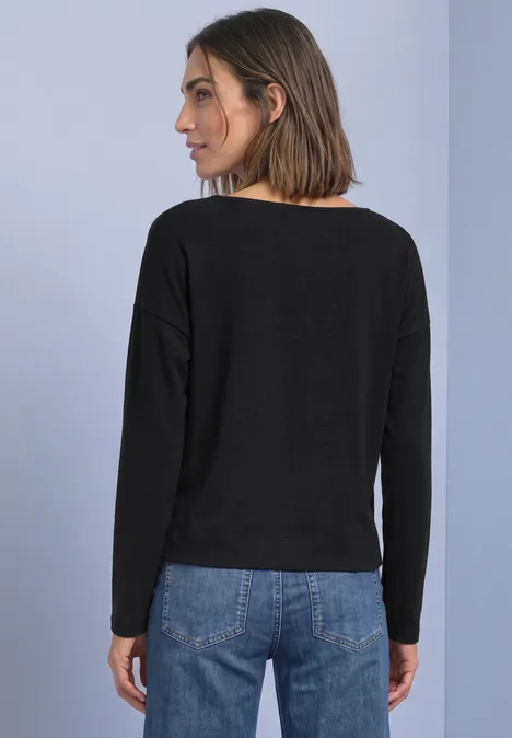 T-shirt à manches longues, col en V et détail en dentelle Black Frau von hinten in schwarzem Langarmshirt und Jeans vor hellem Hintergrund.