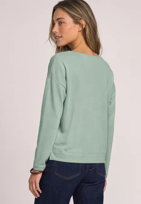 Langarm Shirt mit V-Neck und Spitzendetail eucalyptus green Frau in grünem Pullover und Jeans, Rückenansicht, Blick über die Schulter.