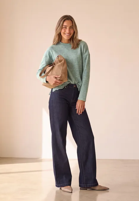 Langarm Shirt mit Rundhals und Spitzenborte eucalyptus green mel. Eine lächelnde Frau trägt mintgrünen Pullover, weite Jeans und hält eine braune Tasche in hellem Raum.