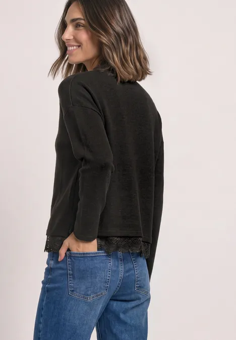 Langarm Shirt mit Rundhals und Spitzenborte black coffee mel. Frau in schwarzem Langarmshirt und blauen Jeans schaut seitlich und lächelt.