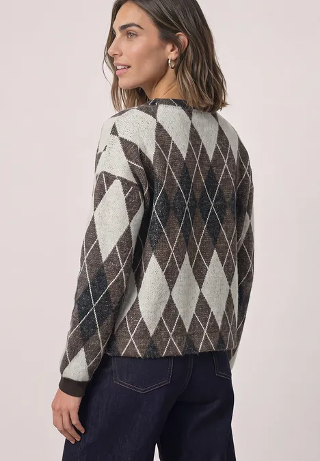Frau mit brünettem Haar trägt argyle Strickpullover und Jeans, blickt seitlich über die Schulter.