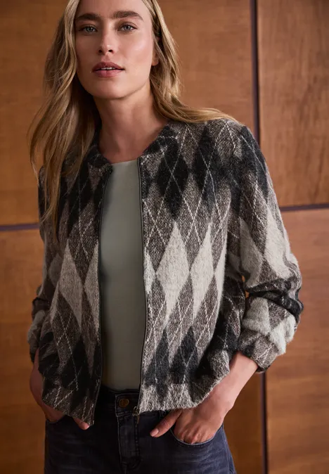 Blouson à manches longues à carreaux black coffee Femme aux cheveux longs porte une veste à motif losange devant un mur en bois.