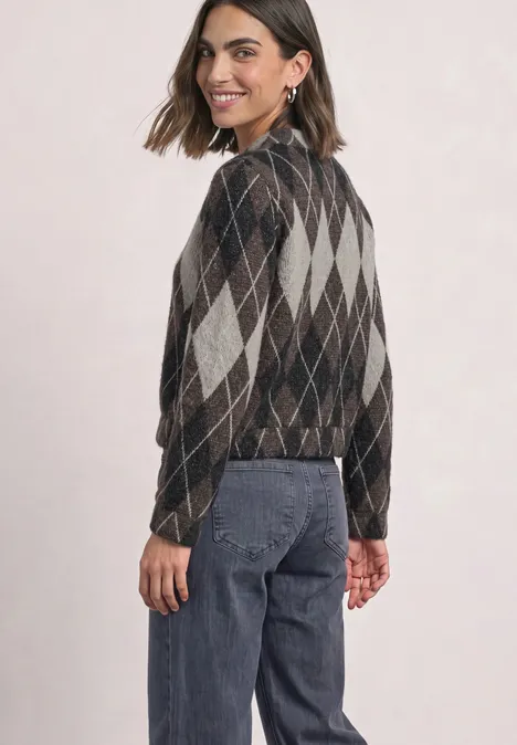 Blouson à manches longues à carreaux black coffee Jeune femme de profil porte un gilet à losanges et un jean, elle sourit légèrement.