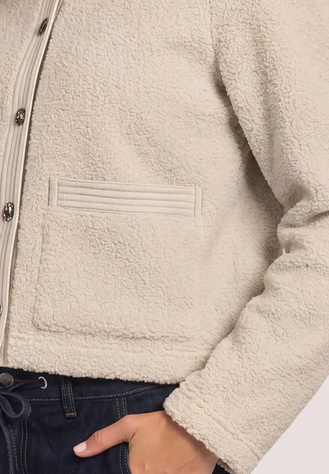 Eine kurze cremefarbene Teddy-Fleecejacke mit Knöpfen und Eingrifftaschen, kombiniert mit dunkler Hose.