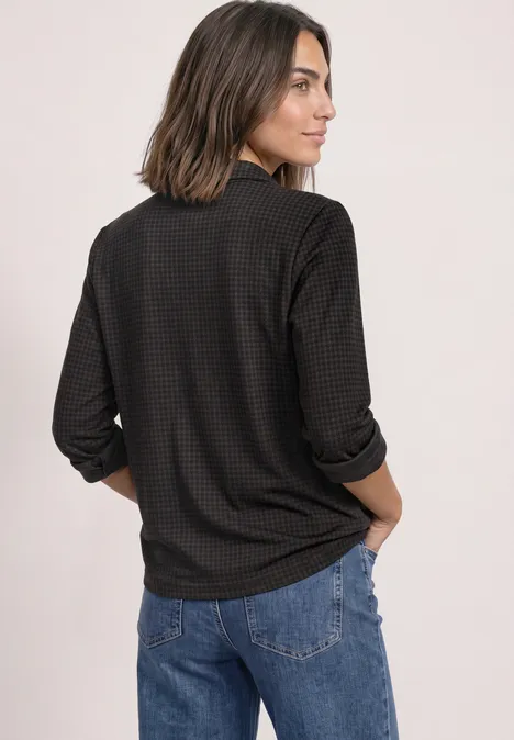 Vrouw van achteren in een donker gemêleerd shirt met lange mouwen en blauwe spijkerbroek, halflang haar.