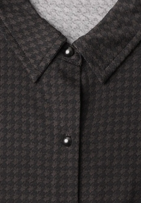 Close-up van een zwart-bruin pied-de-poule overhemdkraag met zilverkleurige knoop.