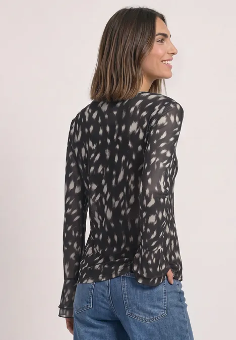 Shirt aus Mesh mit langen Volant-Ärmeln Black Frau in schwarzer, gemusterter Bluse und Jeans, seitlich fotografiert.