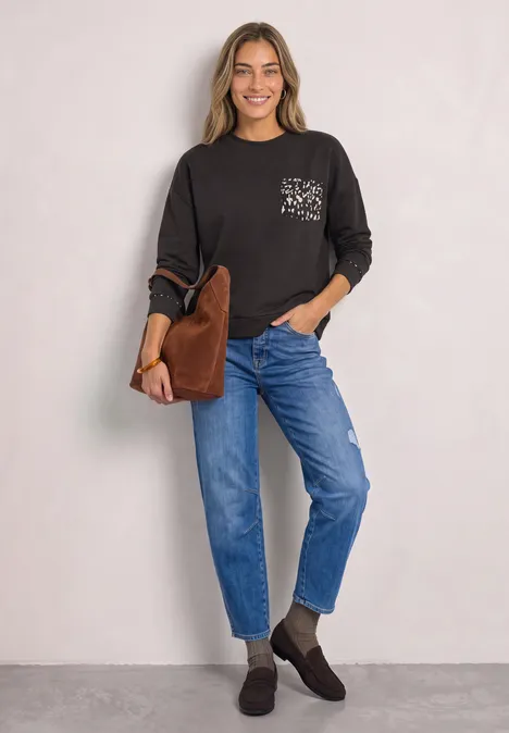 Langarm Shirt mit Rehprint-Details black coffee Eine lächelnde Frau trägt ein schwarzes Langarmshirt, blaue Jeans, braune Stiefeletten und eine braune Tasche.