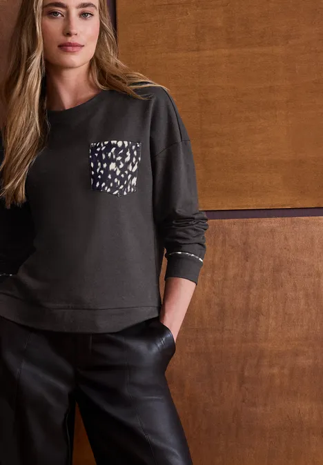 Langarm Shirt mit Rehprint-Details black coffee Frau trägt schwarzen Pullover mit Muster-Tasche und schwarze Lederhose vor Holzpaneel.