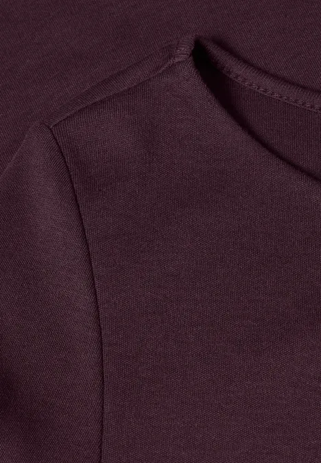 Close-up van een bordeauxkleurig kledingstuk met zichtbare schouder- en halsnaad.