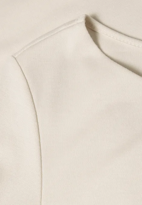 Close-up van een crèmekleurige top met ronde hals en schoudernaad.
