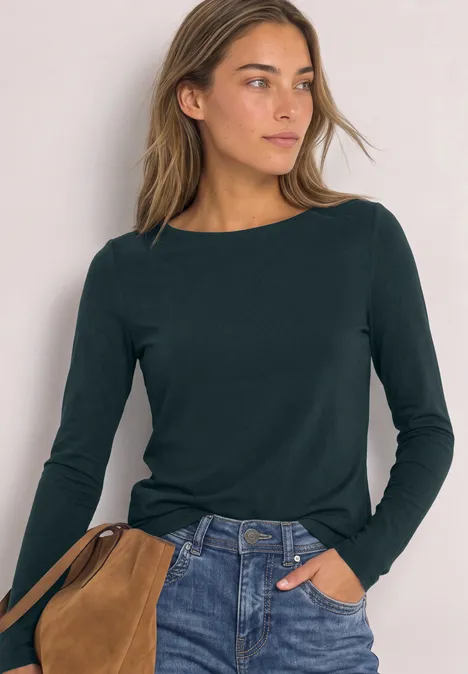 T-shirt basique à col bateau stormy green Junge Frau mit dunkelgrünem Langarmshirt und Jeans, trägt eine braune Schultertasche.