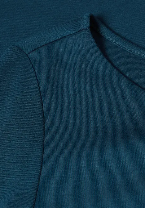 Close-up van een petrolkleurig T-shirt met zichtbare schouder- en halsnaad.