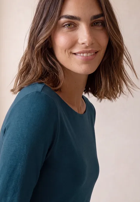 Portret van een glimlachende vrouw met bruin haar en blauw shirt voor een lichte achtergrond.