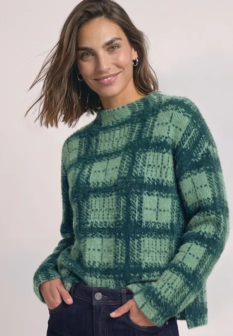 Vrouw lacht in groen geruit trui, hand in de zak.
