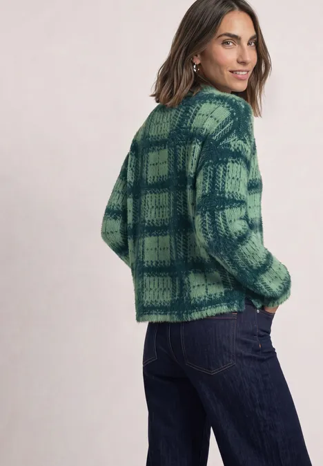 Vrouw in groen-blauw geruit gebreid vest en spijkerbroek, kijkt over haar schouder.