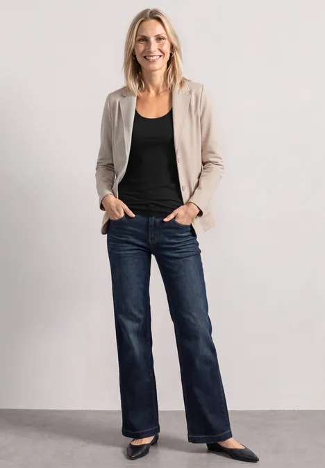 Haut long à col rond et dentelle à l'ourlet Black Eine lächelnde Frau steht in blauer Jeans, schwarzem Oberteil, beigem Blazer und schwarzen Schuhen.