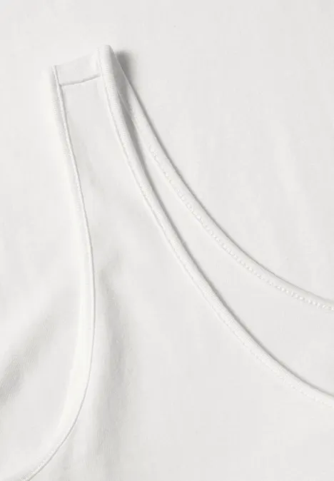 Haut long à col rond et dentelle à l'ourlet off white Nahaufnahme eines weißen Tanktops mit Rundhalsausschnitt auf hellem Untergrund.