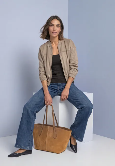 Haut long à col rond et dentelle à l'ourlet black coffee Frau sitzt auf weißem Würfel, trägt beige Jacke, schwarzen Top, weite Jeans und hält braune Tasche.