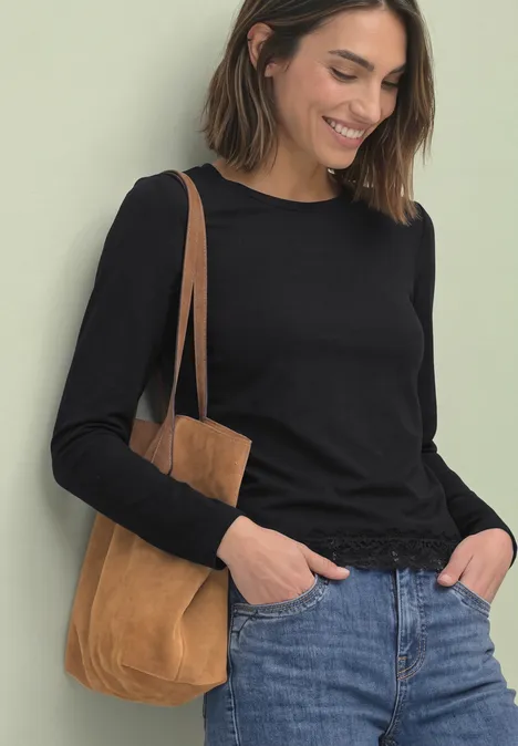 Langarm Shirt mit Rundhals und Spitzenkante Black Frau in schwarzem Langarmshirt und Jeans mit brauner Wildleder-Umhängetasche, lächelnd.