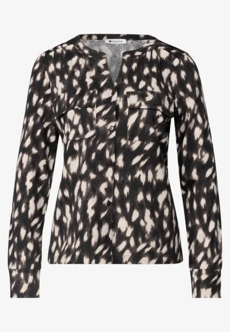 Schwarze Bluse mit cremefarbenem Tupfenmuster, V-Ausschnitt und langen Ärmeln.