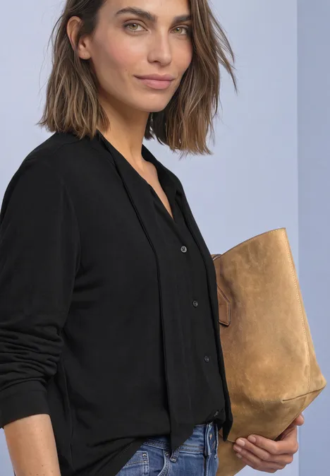 Frau mit schulterlangem braunem Haar in schwarzem Cardigan, die eine beige Clutch hält.