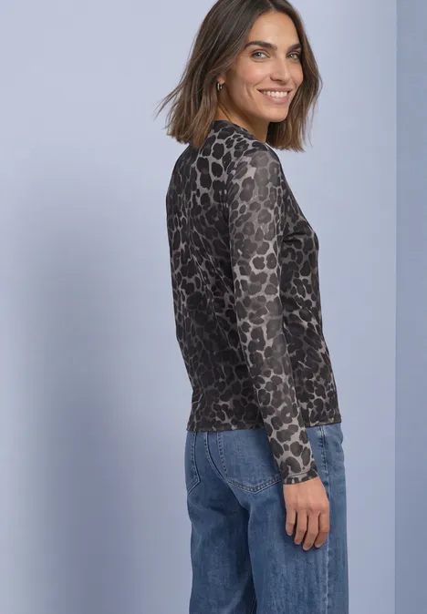 Vrouw in shirt met luipaardprint en lange mouwen en jeans, voor paarse achtergrond.